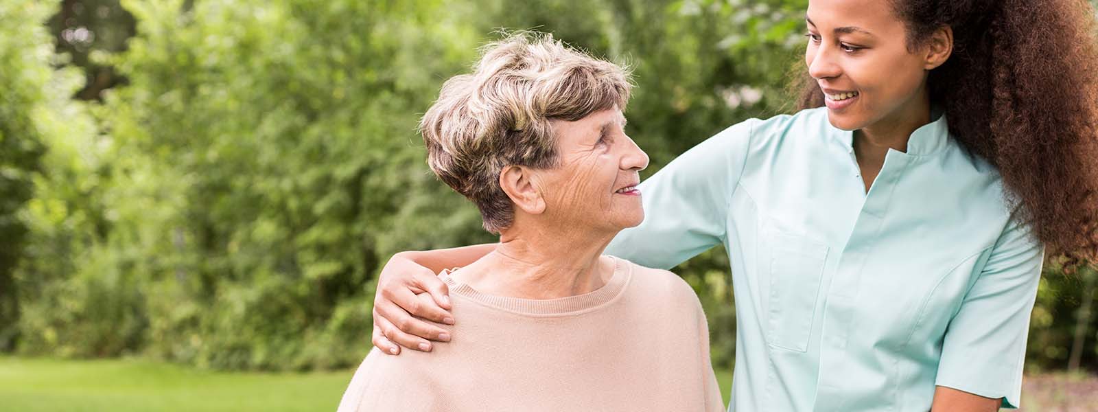 Panorama of young female afroamerican caregiver supporting elderly woman